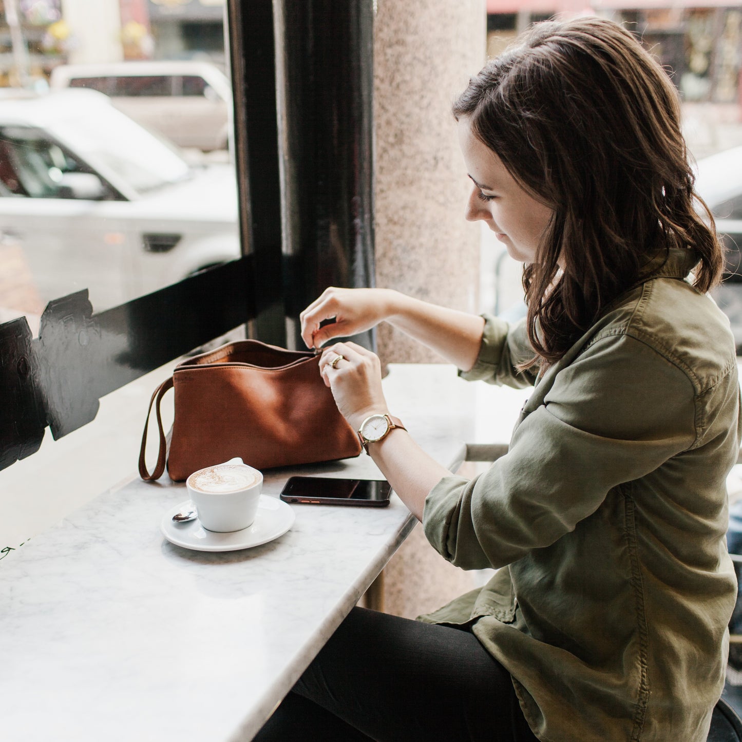 A woman zipping up the Miina Leather Toiletry Bag, emphasizing its smooth zipper closure and stylish, functional design.