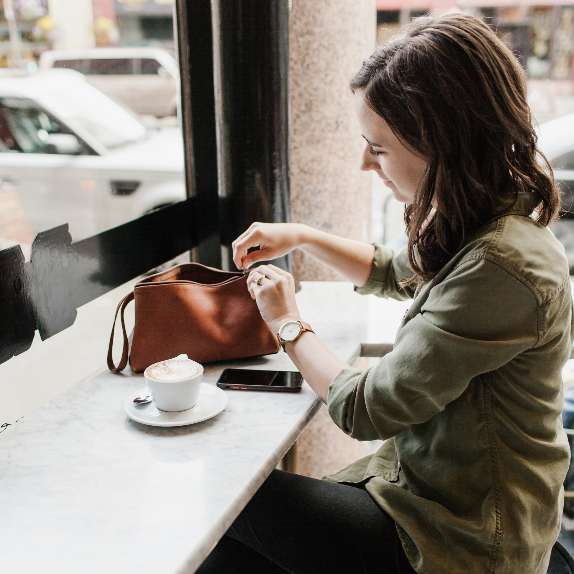 A woman zipping up the Miina Leather Toiletry Bag, emphasizing its smooth zipper closure and stylish, functional design.