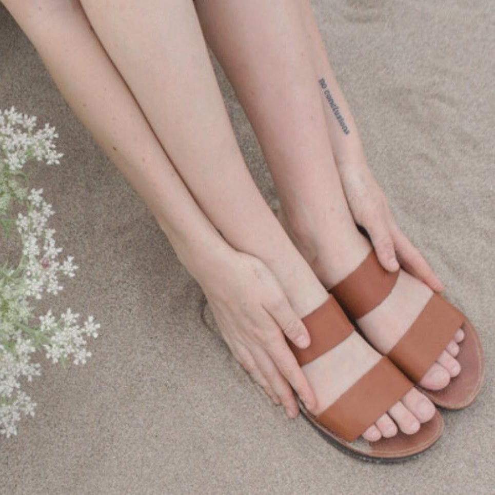 Model's feet on the beach wearing the Ophelia slide sandal in caramel